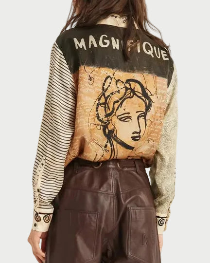 A model is shown from the back wearing a vintage-style graphic jacket with 'MAGNIFIQUE' text and a portrait illustration, paired with brown faux-leather trousers and black ankle boots, against a plain white studio background.