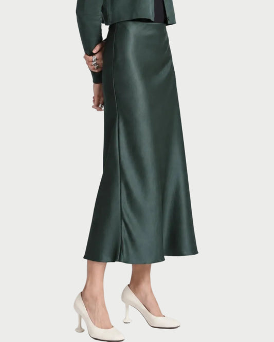 A person wears a forest green Saint Art Talia Maxi Skirt Forest bias-cut maxi skirt and white heels.