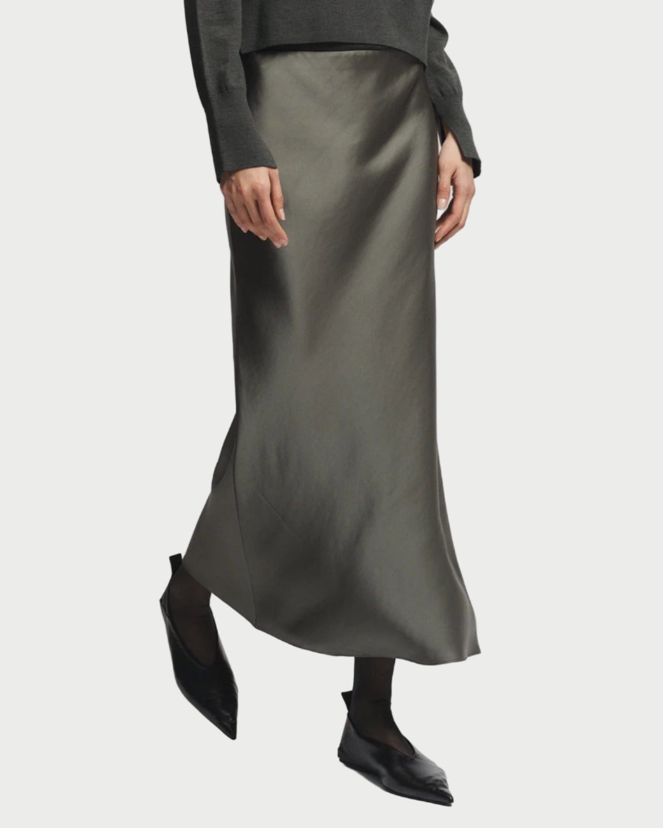 Person wearing a dark green sweater and satin skirt on a light gray background