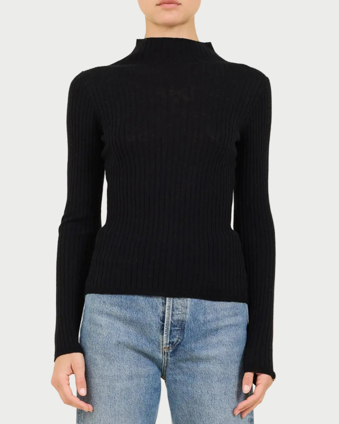 Person wearing a black ribbed turtleneck sweater and light blue jeans on a beige background
