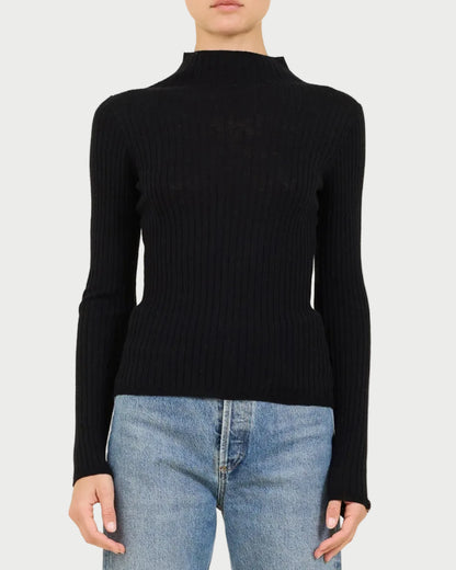 Person wearing a black ribbed turtleneck sweater and light blue jeans on a beige background