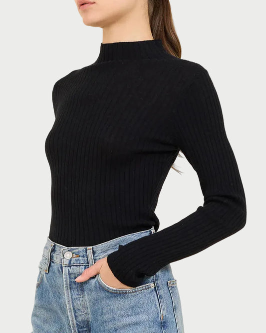 Person wearing a black ribbed turtleneck and blue jeans on a beige background
