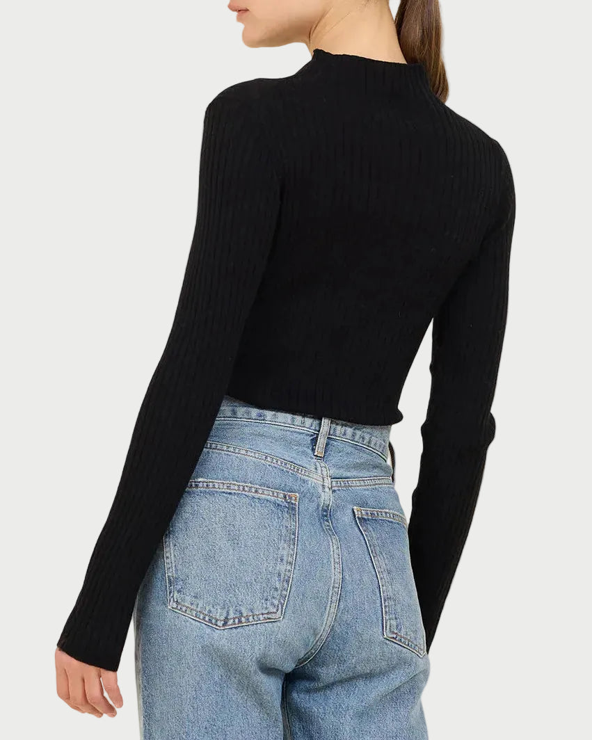 Person wearing a black ribbed sweater and blue jeans on a beige background