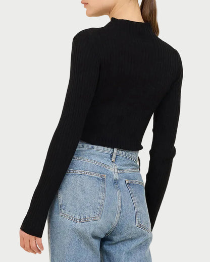 Person wearing a black ribbed sweater and blue jeans on a beige background