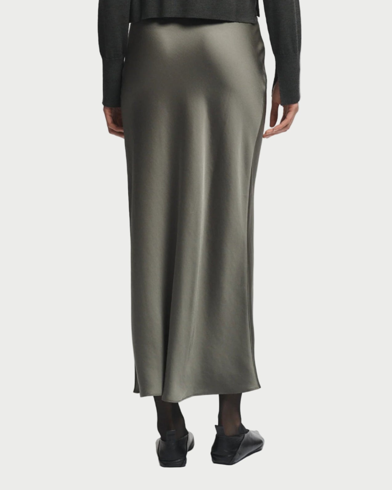 Person wearing a green sweater and long satin skirt on a white background