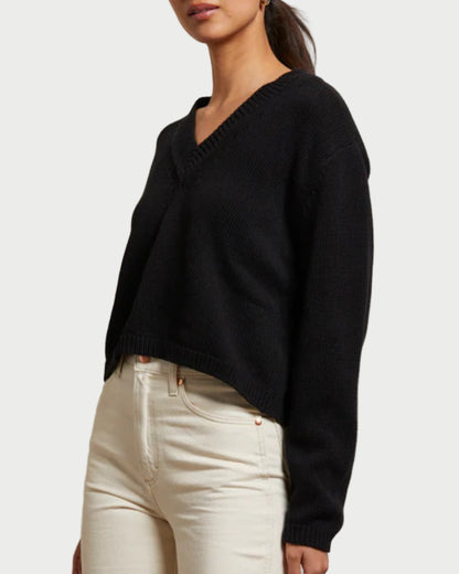 Woman wearing a black sweater and white pants against a plain background