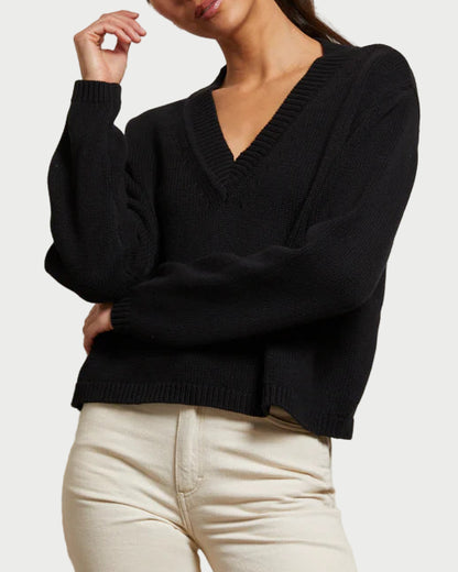 Woman wearing a black sweater and white pants against a plain background