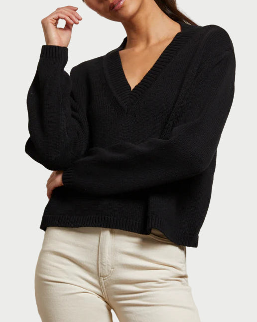 Woman wearing a black sweater and white pants against a plain background