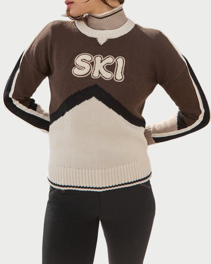 Person wearing a sweater with 'SKI' text by a snowy mountain lake