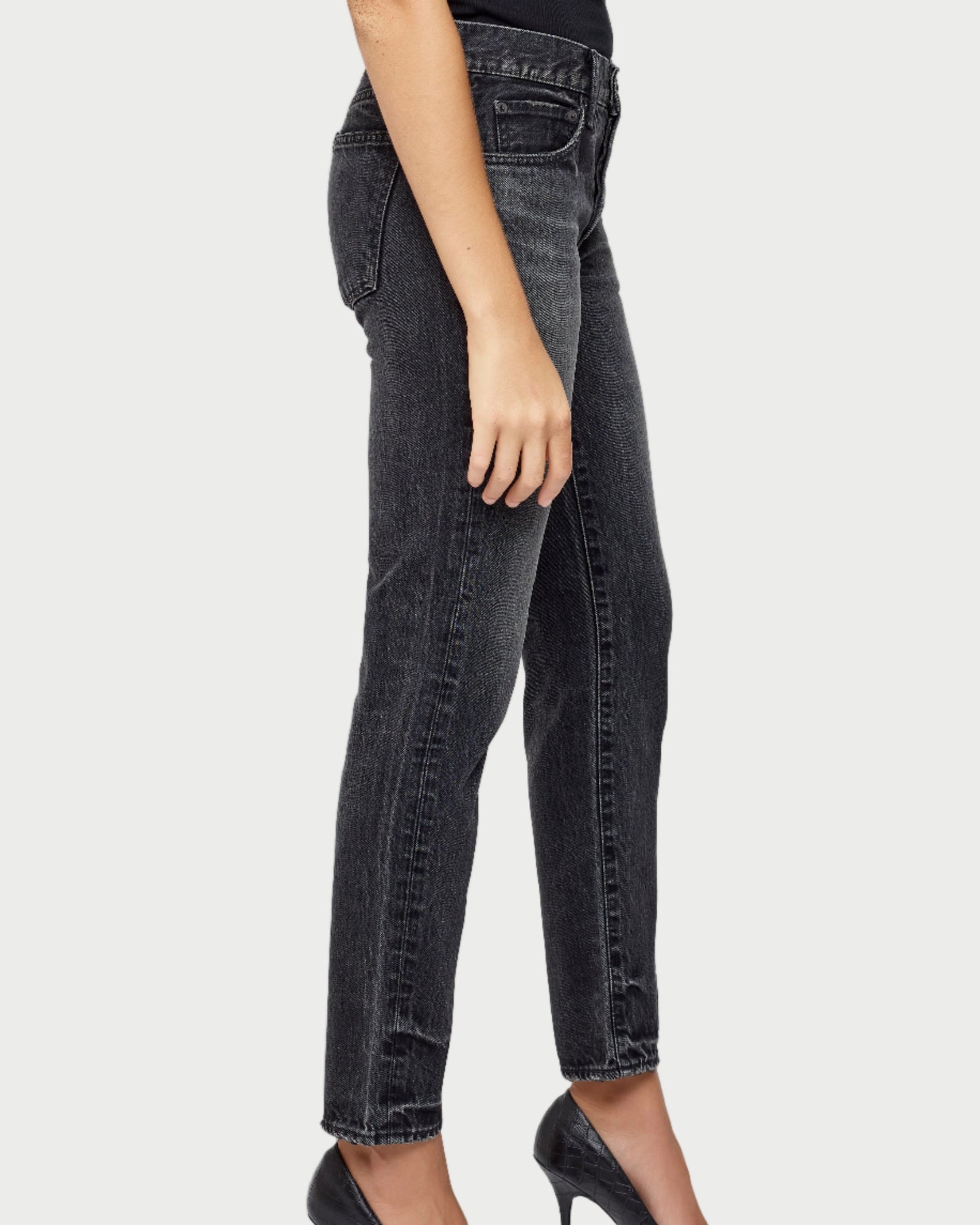 Person wearing black jeans and black high-heeled shoes on a light gray background