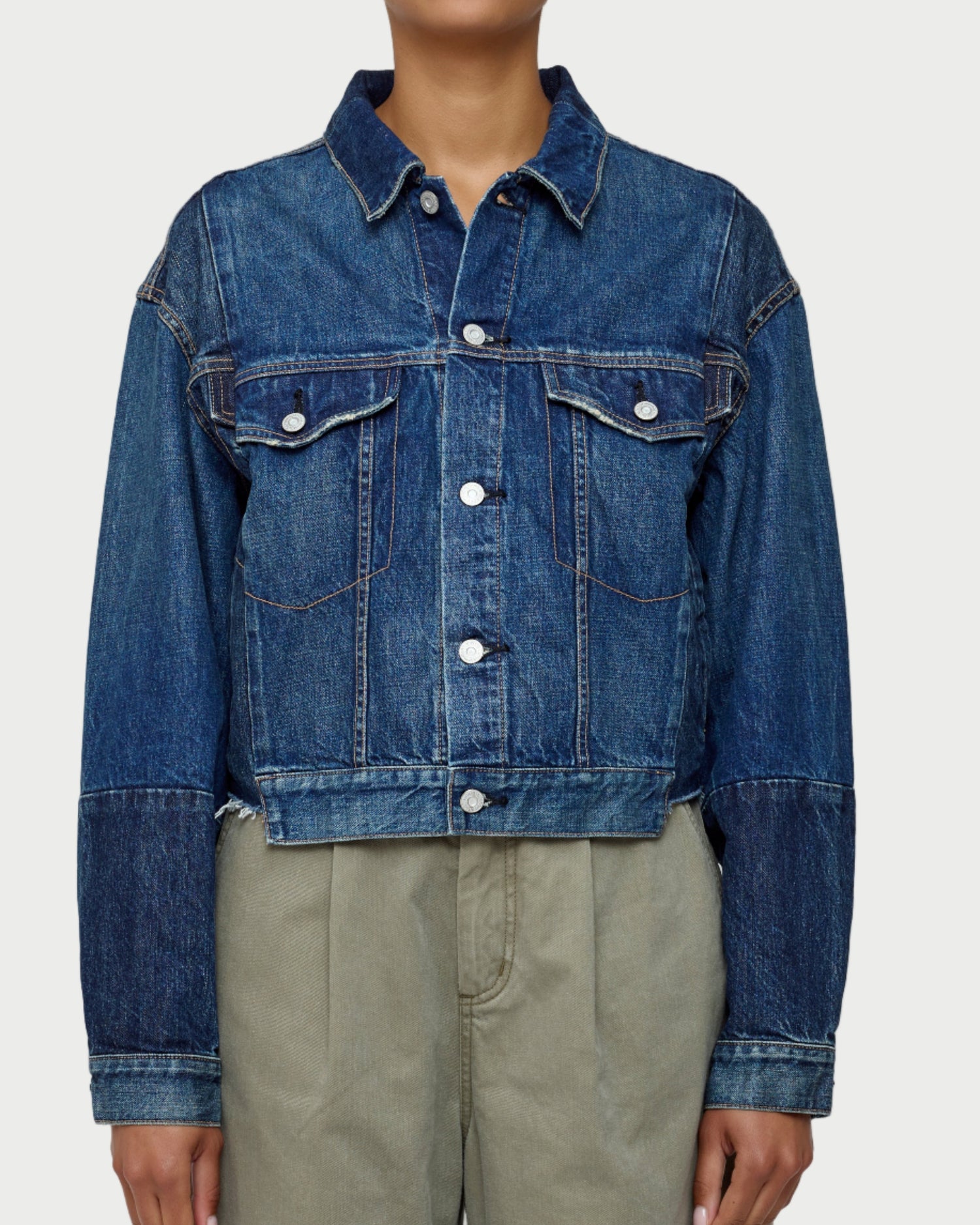 Person wearing a blue denim jacket and beige pants on a white background