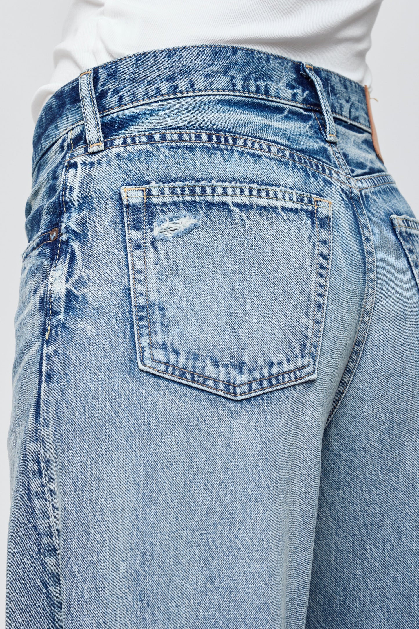 Close-up of the back of a person wearing Moussy’s Lewes Super Wide Jeans in light blue Japanese cotton, featuring a high waist, slightly distressed back pocket, and faded detailing, paired with a white top.