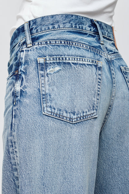 Close-up of the back of a person wearing Moussy’s Lewes Super Wide Jeans in light blue Japanese cotton, featuring a high waist, slightly distressed back pocket, and faded detailing, paired with a white top.