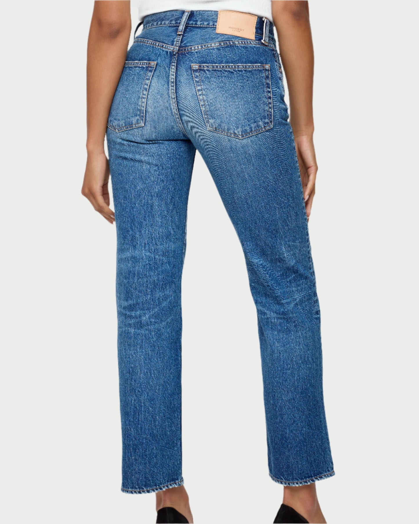 A person seen from behind wearing Moussy Sunset Straight Jeans in Japanese cotton denim, featuring visible back pockets, a tan leather patch, slightly faded texture, mid-rise straight leg fit, and raw hems at the ankles.