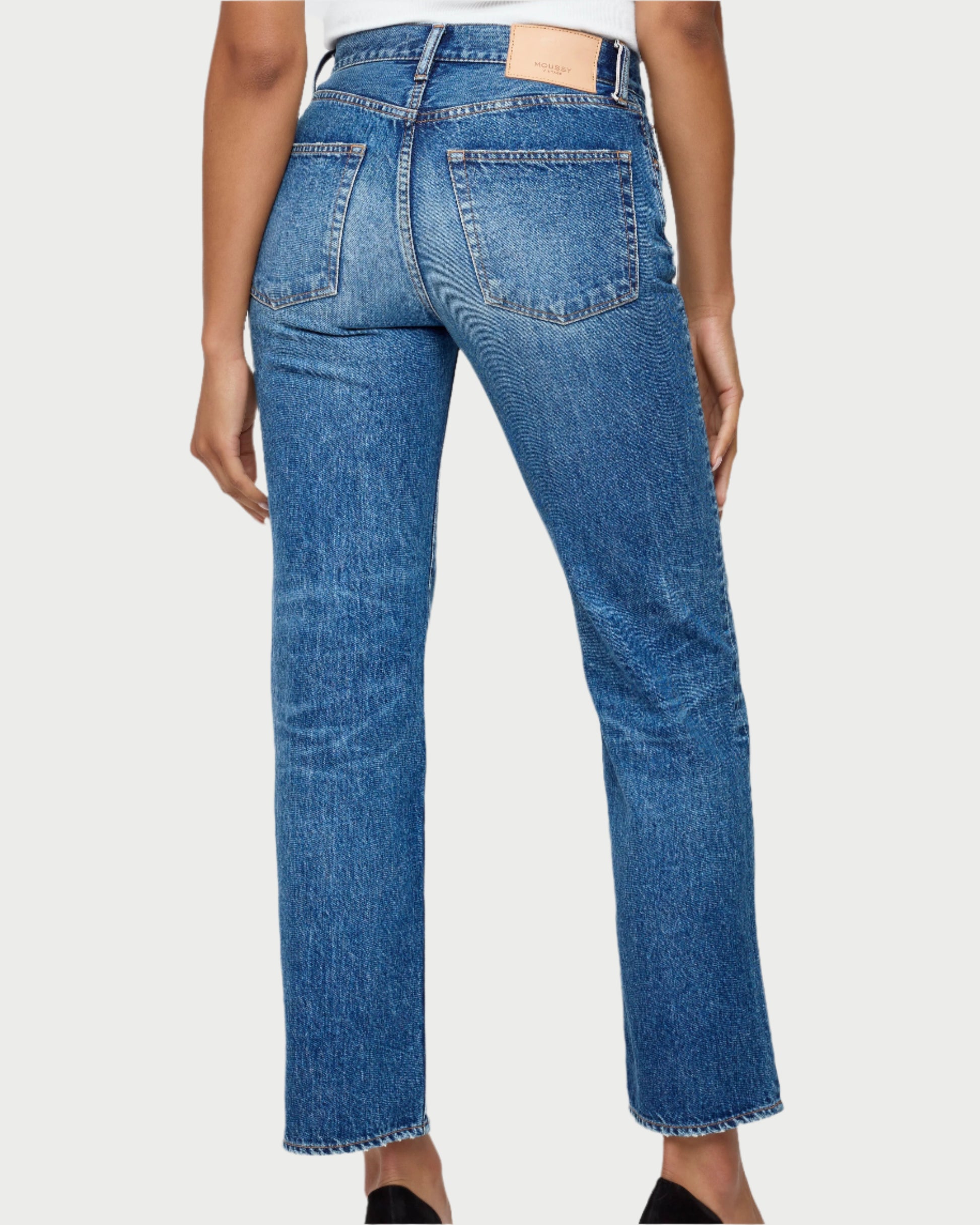 A person seen from behind wearing Moussy Sunset Straight Jeans in Japanese cotton denim, featuring visible back pockets, a tan leather patch, slightly faded texture, mid-rise straight leg fit, and raw hems at the ankles.