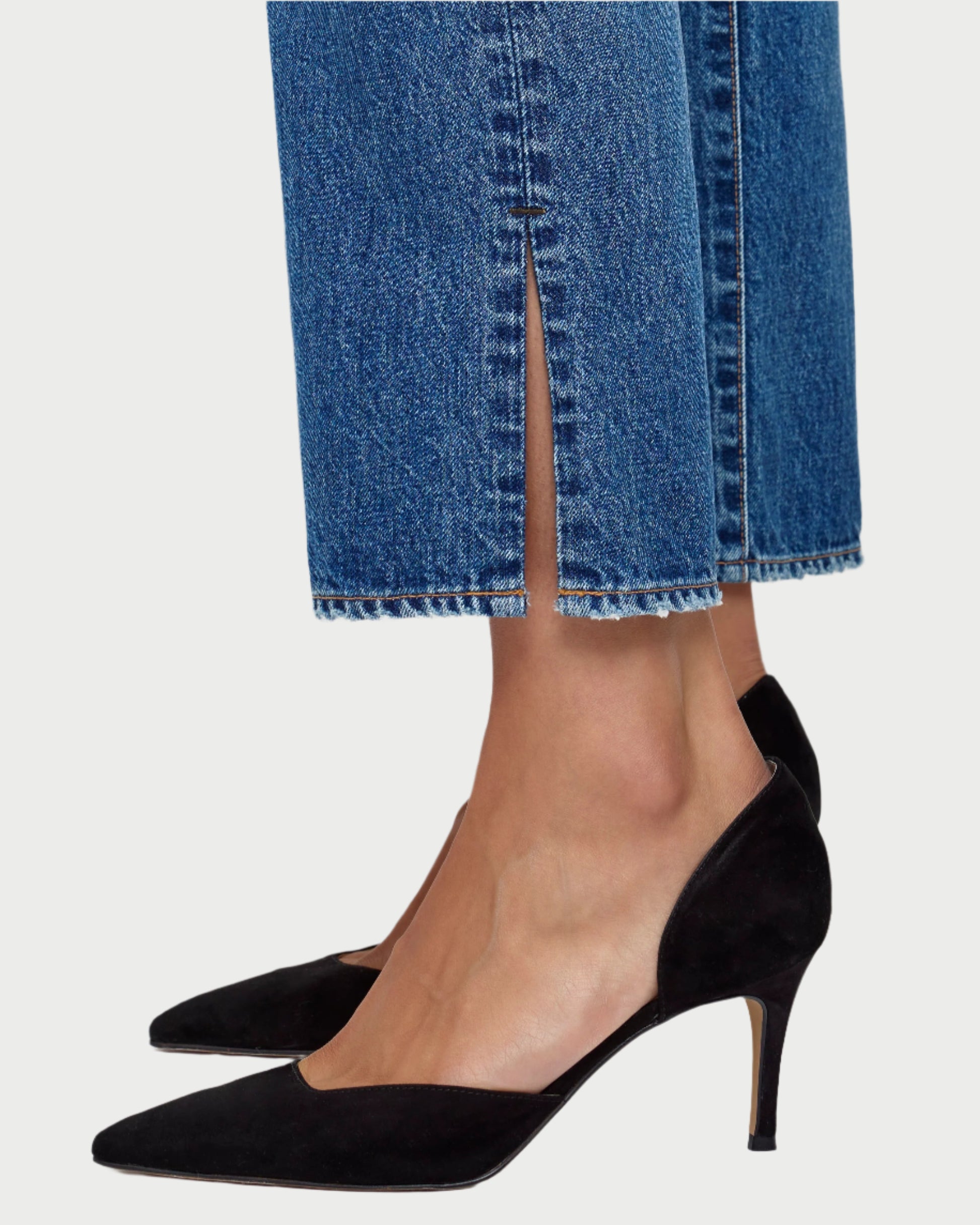 Close-up of a person wearing Moussy Sunset Straight Jeans, made from Japanese cotton denim in a mid-rise straight leg style with a front slit and frayed edge, paired with black pointed-toe kitten heels.