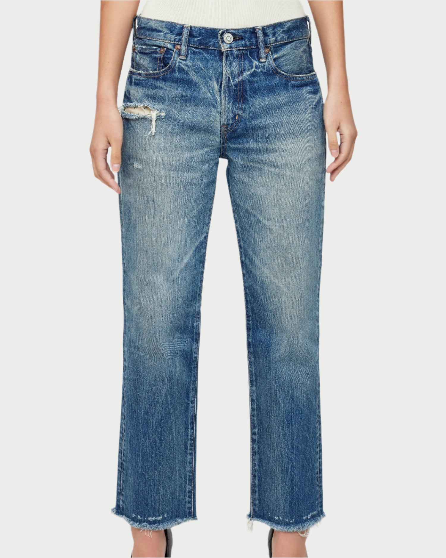 Someone is wearing Moussy's Sayville Boys Jeans, which are blue distressed boy-fit jeans made from Japanese denim, featuring a ripped detail near the front pocket. These mid-rise jeans have a raw hem and straight-leg fit, paired seamlessly with a tucked-in white top against a plain light background.