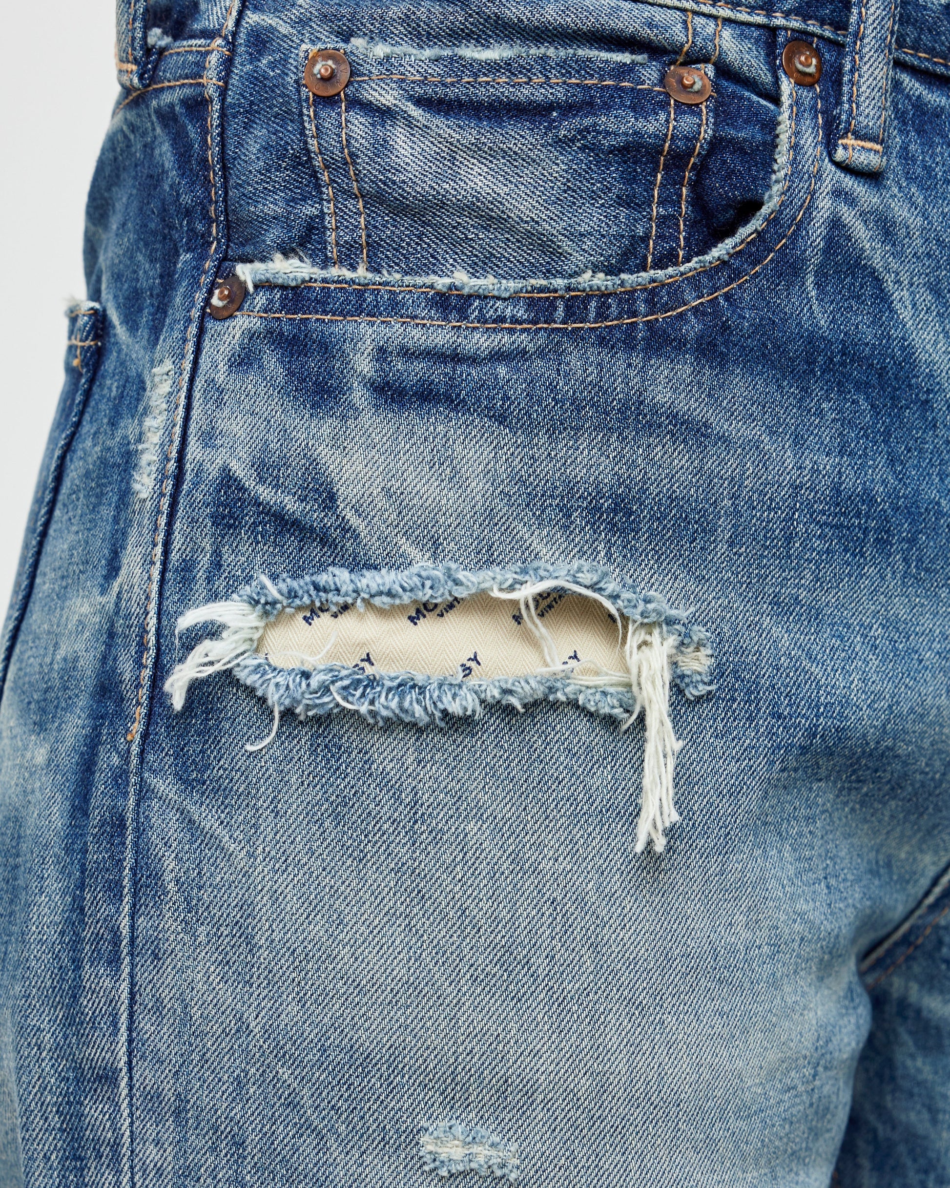A close-up reveals a frayed tear on the front pocket of Moussy's Sayville Boys Jeans. The exposed Japanese denim adds a distressed, vintage vibe, while brass rivets reinforce the nearby area.