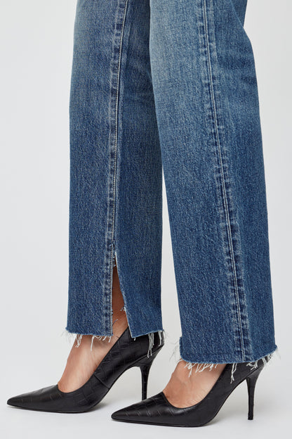 A person wearing Moussy Gleason Straight Leg Jeans with frayed hems and front slits, paired with black pointed-toe heels, stands against a plain white background.