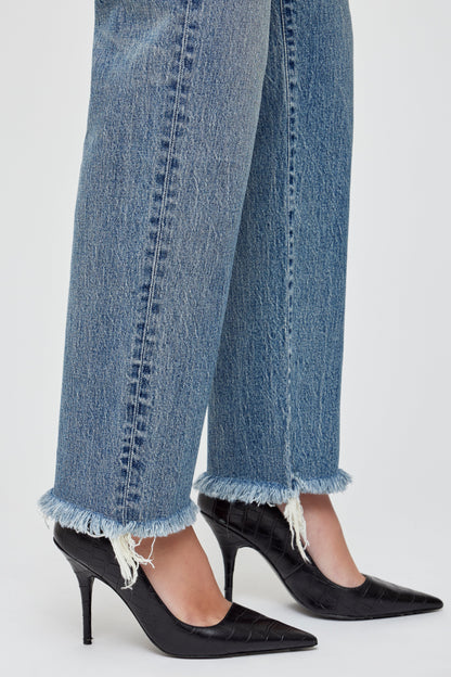 A person wears Moussy Massapequa Straight Leg Jeans with frayed hems and black pointed-toe heels, standing against a light background.