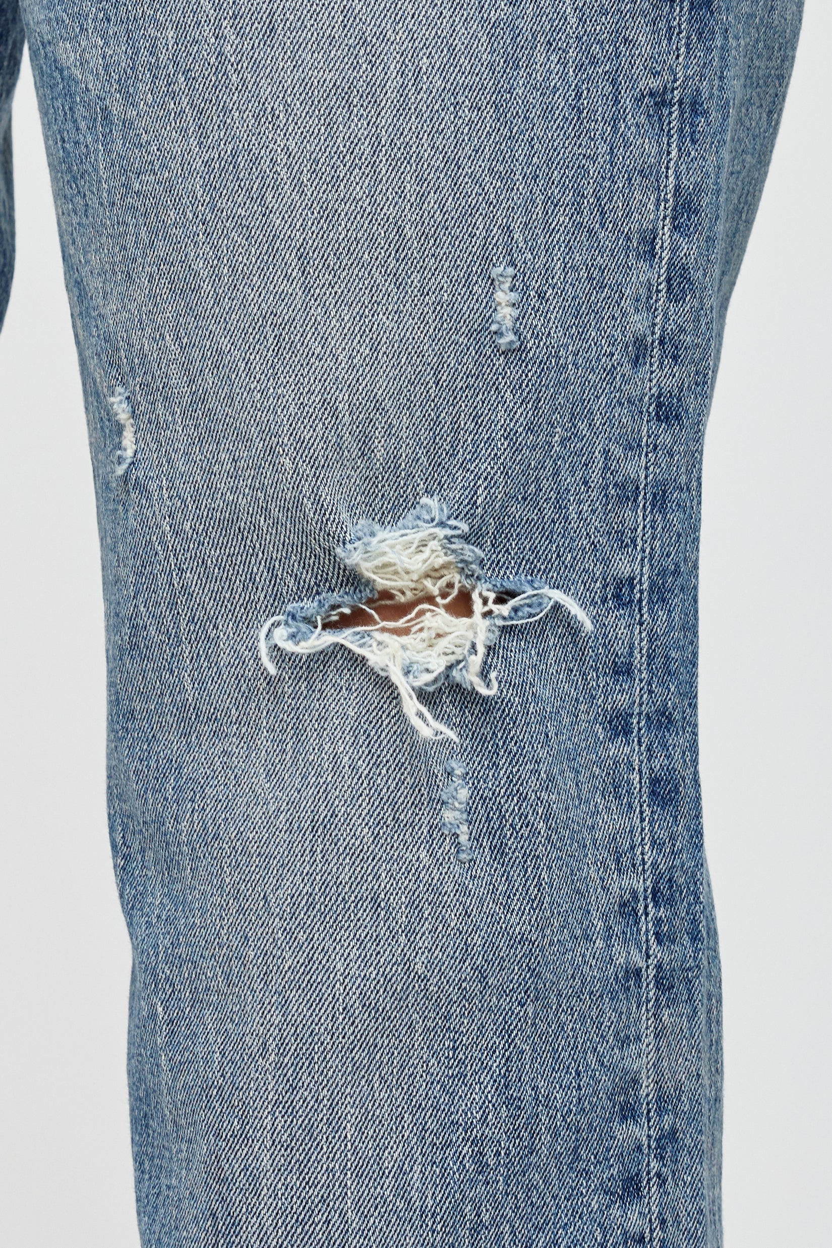 Close-up of the Moussy Massapequa Straight Leg Jeans, featuring a large frayed hole on the thigh and smaller distressed patches that reveal white threads and some skin beneath.
