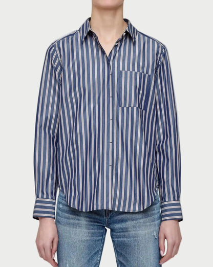 Person wearing a blue and white striped shirt with a pocket, standing against a plain background
