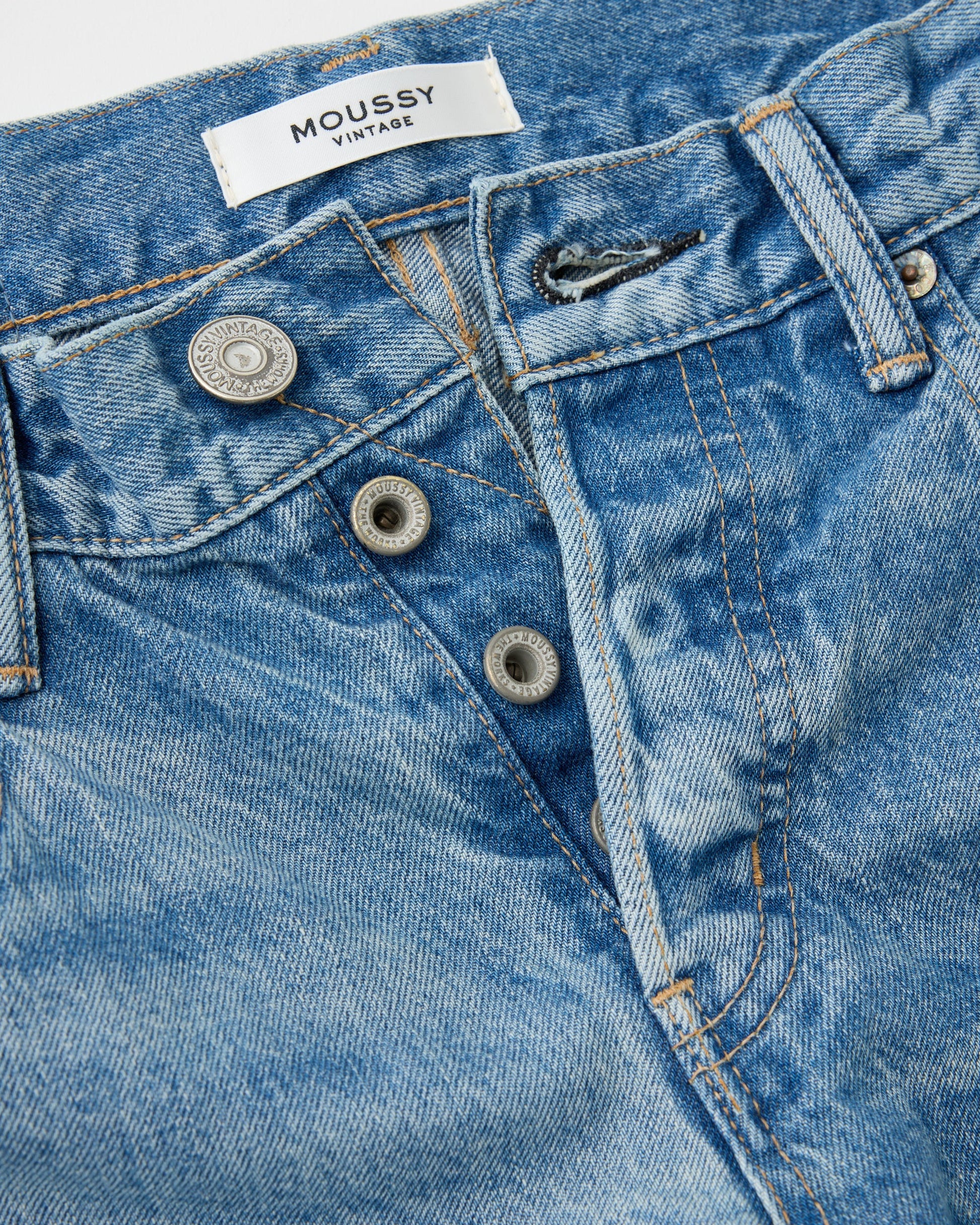 Close-up of blue jeans with a 'MOUSSY' label on a white background