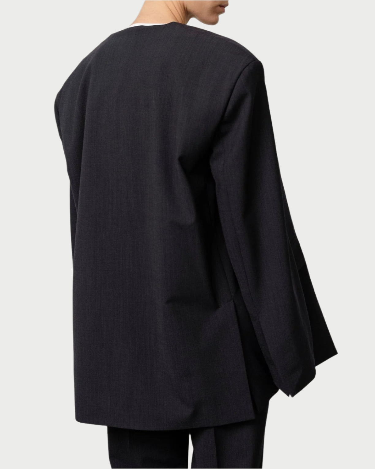 A person wears Herskind’s oversized navy melange wool Indiana Blazer with matching trousers, shown from the back and slightly turned to the side, against a plain light background.