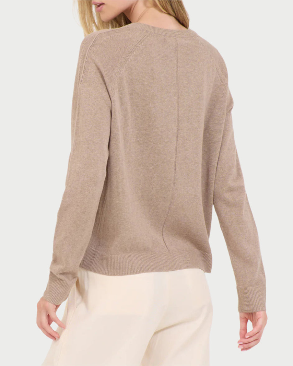 A person is shown from behind wearing the One Grey Day Linen V Neck Sweater in beige, featuring long sleeves and a simple design. Paired with white pants, this linen/cotton blend outfit shines against a plain background.