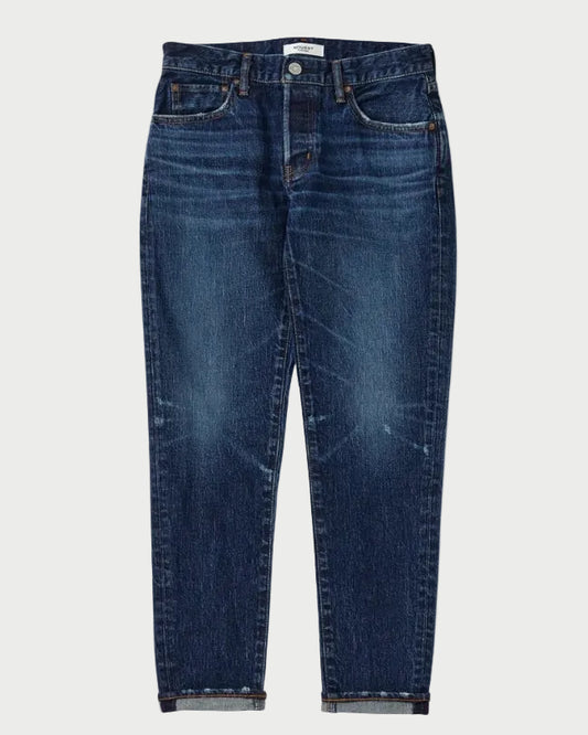 A pair of dark blue denim jeans with a tapered, cropped fit and rolled cuffs, shown flat against a light gray background.