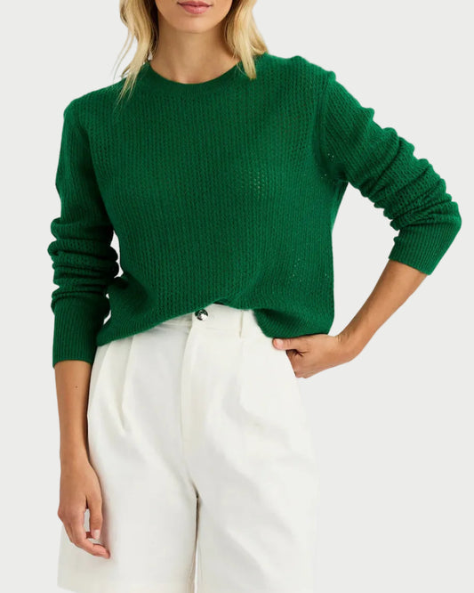 Woman wearing a green sweater and white shorts on a plain background