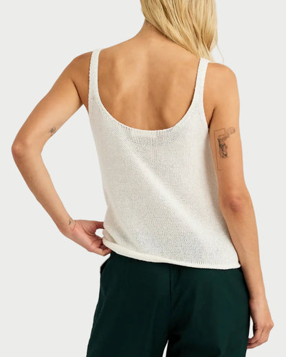 Person wearing a white sleeveless top and dark green pants on a light gray background