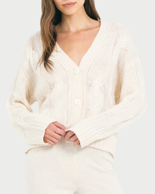 Woman wearing a cream-colored cable knit sweater on a white background