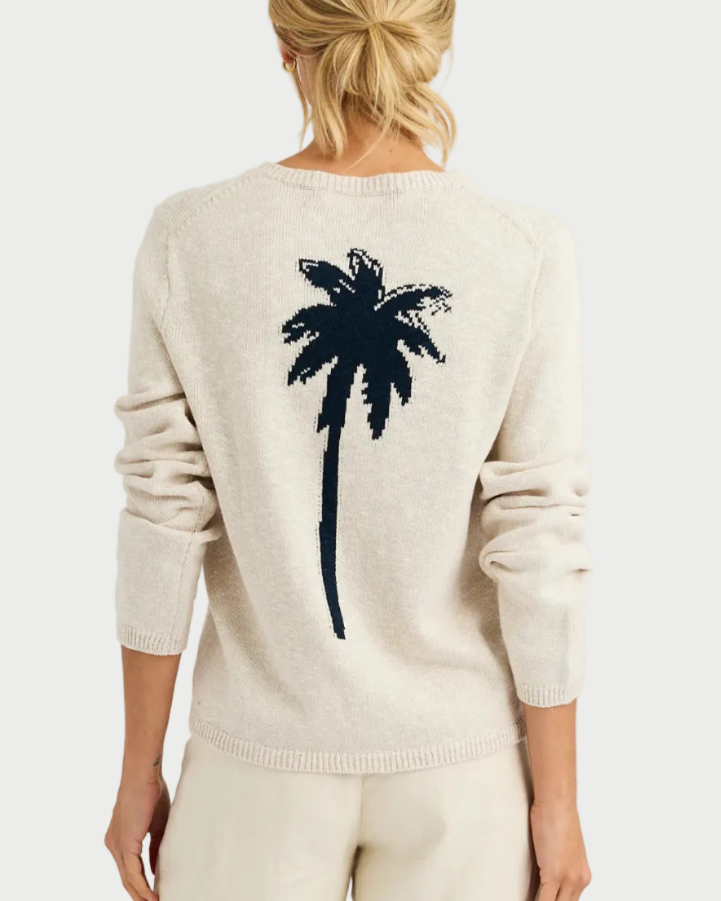 Person wearing a cream sweater with a palm tree design on the back against a white background