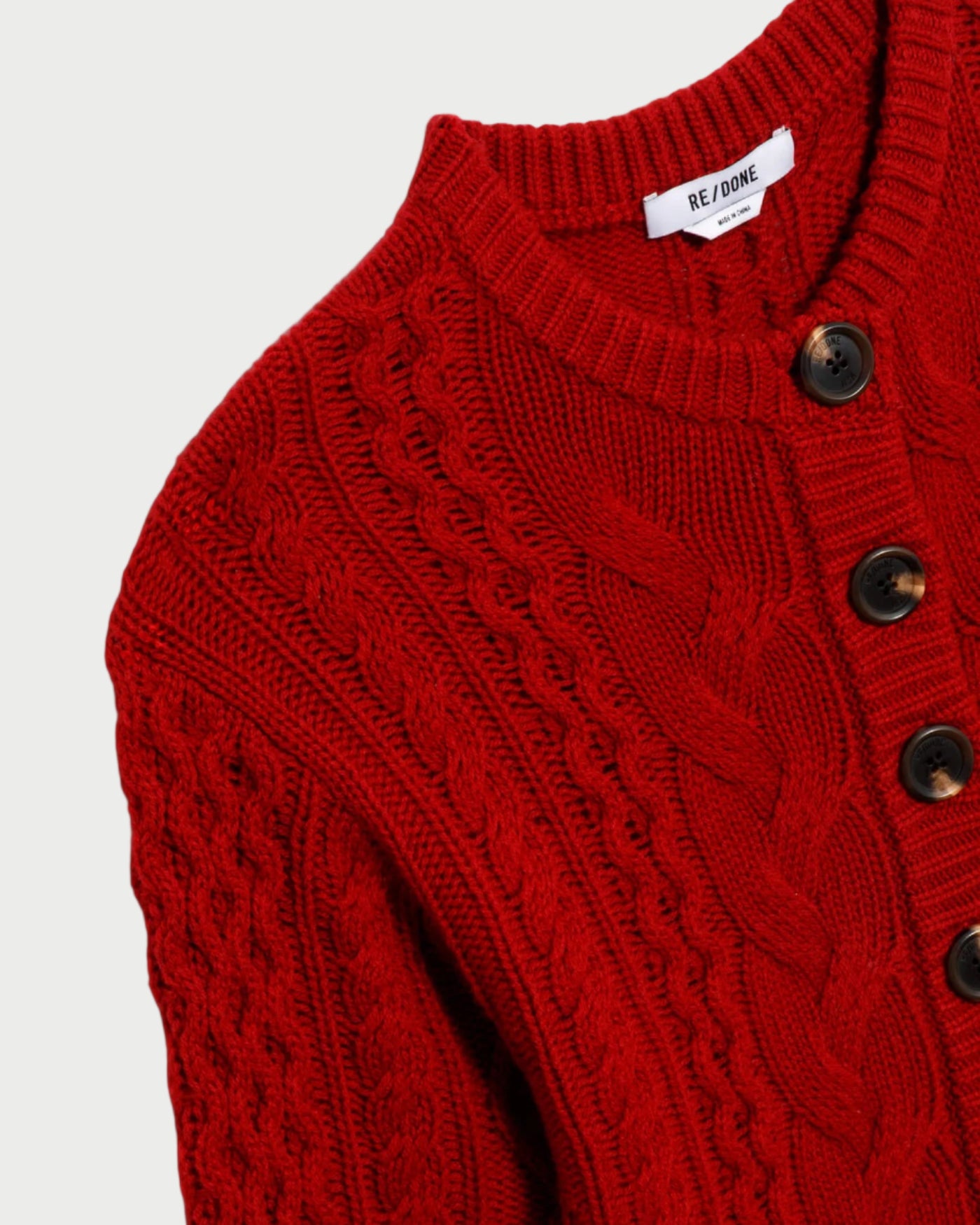Close-up of a red knitted cardigan with button details on a light gray background