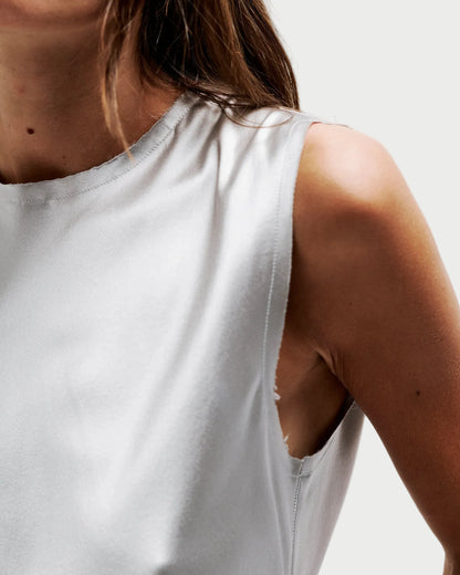 Close-up of a model wearing a light gray sleeveless top with a unique side cutout detail, set against a plain light gray background.