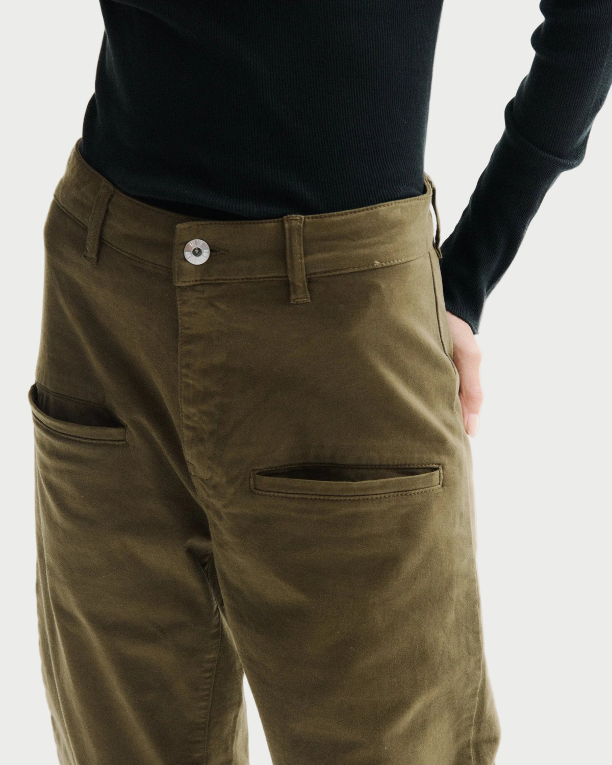 Close-up of a person wearing olive green trousers with a black long-sleeve top, showing the back pocket and side pocket details against a plain white background.