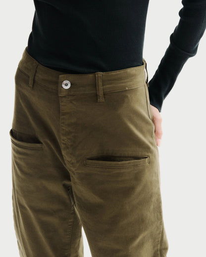 Close-up of a person wearing olive green trousers with a black long-sleeve top, showing the back pocket and side pocket details against a plain white background.