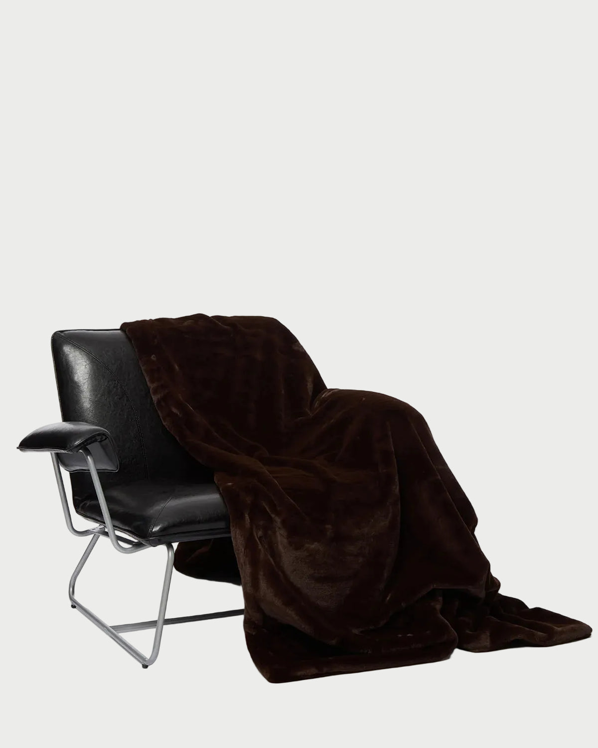 An espresso Apparis Brady Blanket in dark brown faux fur draped over a black leather armchair.
