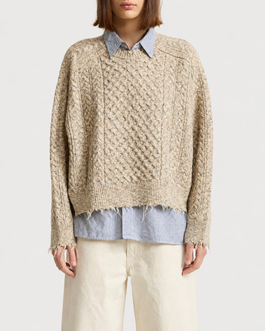 A beige Denimist Oversized Cropped Sweater with a boxy fit and a distressed, frayed hem layered over a blue and white striped collared shirt.