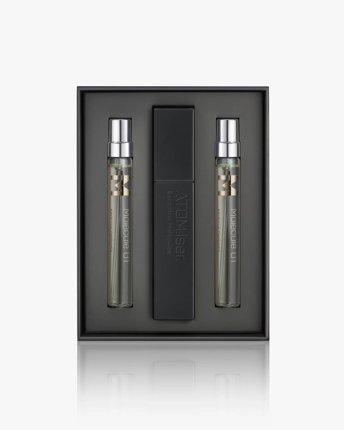 The Escentric Molecules Atomizer set by Escentric Molecules includes two slim "Molecule 01" spray bottles and a sleek black travel case with a twist-and-spray mechanism, all arranged in a minimalist dark tray.