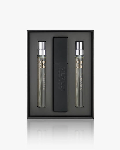 The Escentric Molecules Atomizer set by Escentric Molecules includes two slim "Molecule 01" spray bottles and a sleek black travel case with a twist-and-spray mechanism, all arranged in a minimalist dark tray.