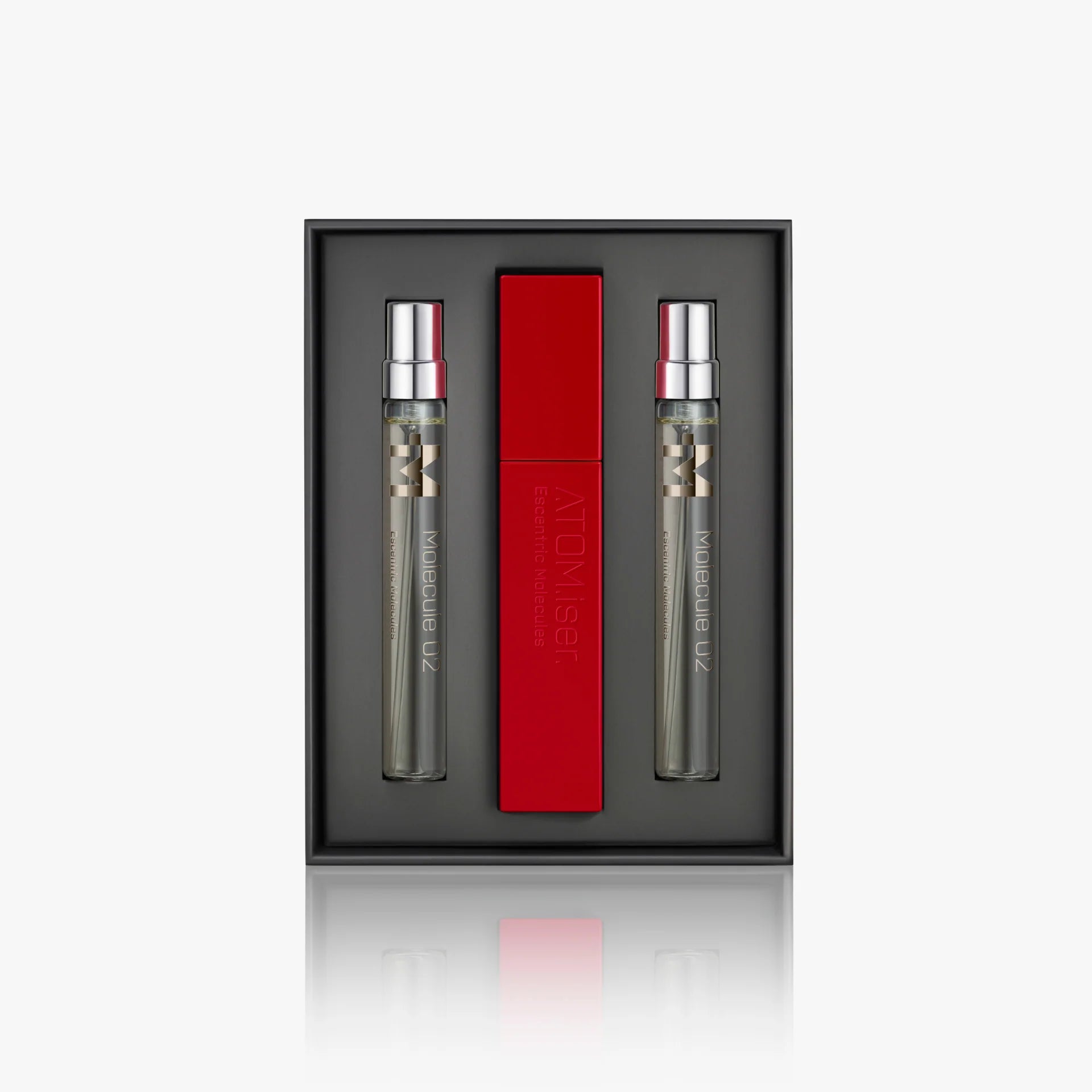 The Escentric Molecules Atomizer gift set by Escentric Molecules includes two clear perfumes with silver caps and a red travel-sized Atomizer case, all elegantly displayed against a dark backdrop.