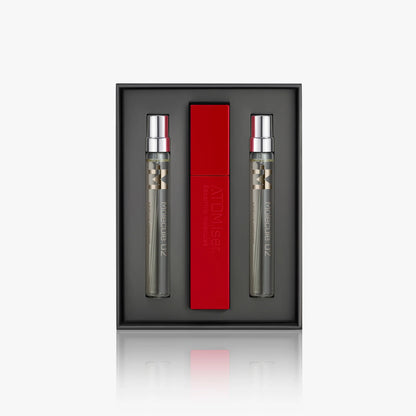 The Escentric Molecules Atomizer gift set by Escentric Molecules includes two clear perfumes with silver caps and a red travel-sized Atomizer case, all elegantly displayed against a dark backdrop.
