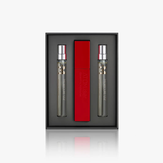 The Escentric Molecules Atomizer gift set by Escentric Molecules includes two clear perfumes with silver caps and a red travel-sized Atomizer case, all elegantly displayed against a dark backdrop.