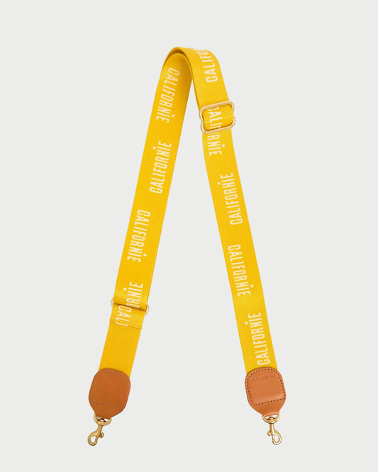 The Clare V. Californie Adjustable Crossbody Strap by CLARE V. features a yellow strap with "CALIFORNIE" in white, brown leather ends, and gold clasps for easy bag attachment.