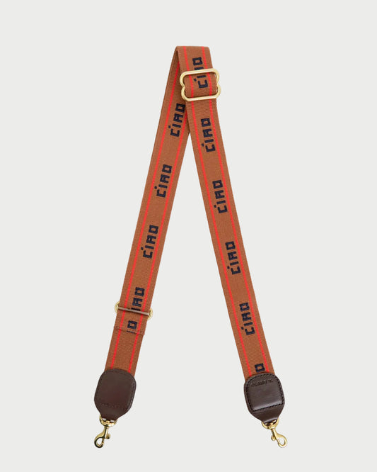 Clare V. Ciao Adjustable Crossbody Strap featuring a repeating red stripe and the word “CIAO” in black text, finished with brass hardware and dark brown leather end tabs with swivel clips.