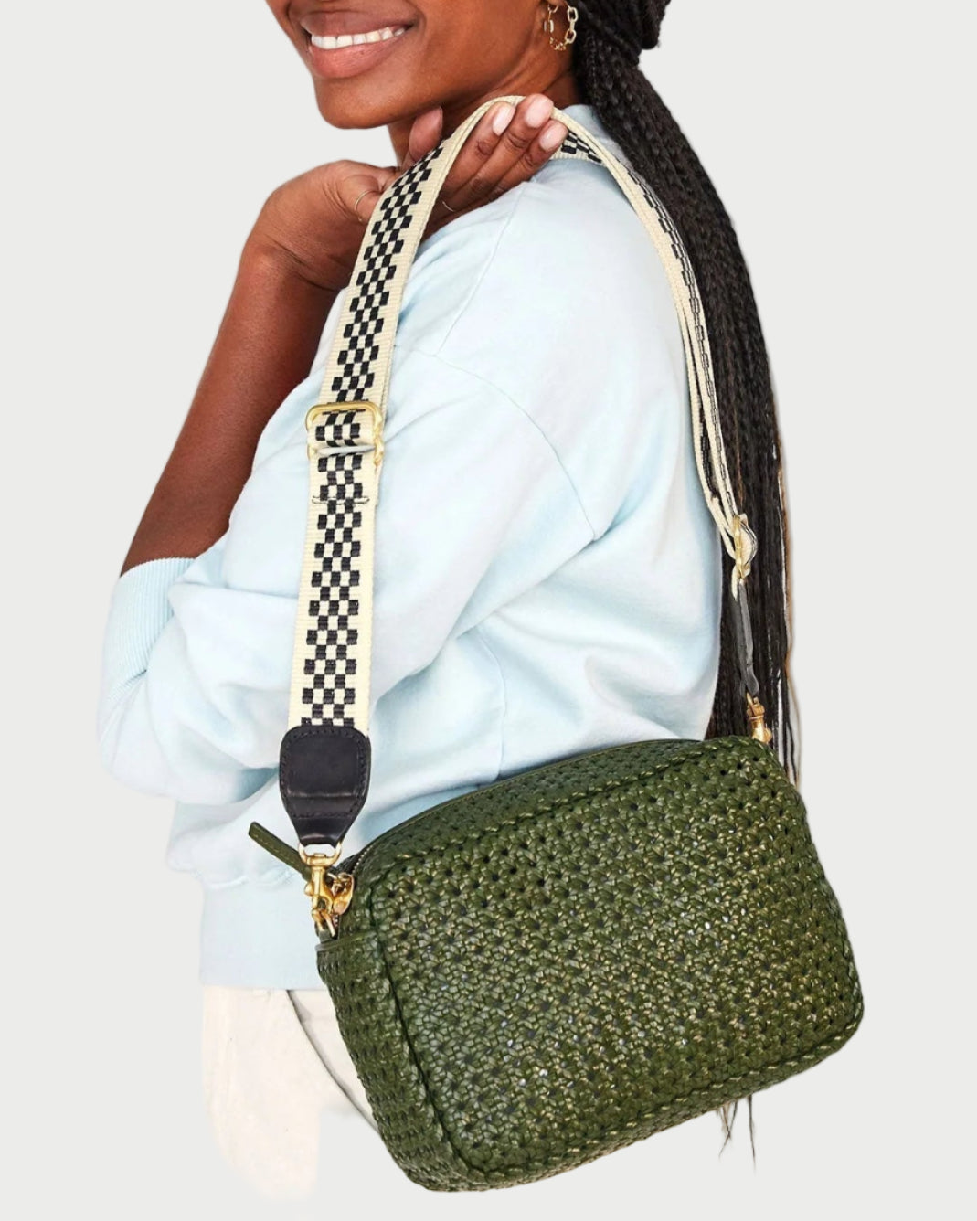 Woman holding a green woven handbag with a checkered strap against a white background