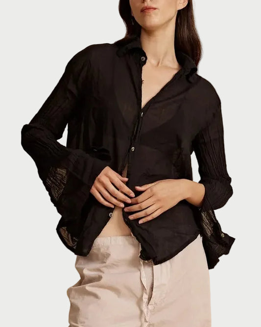 Woman wearing a black blouse and beige pants against a beige background