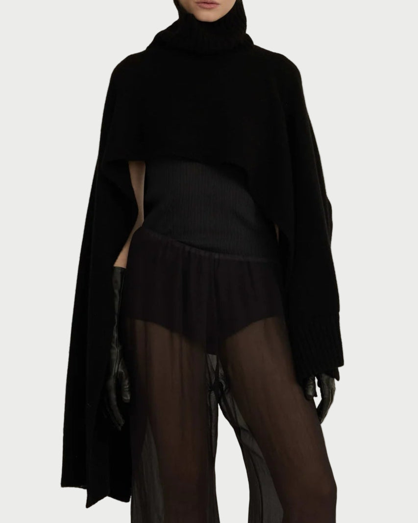 Person wearing a black turtleneck and skirt with sheer leggings on a neutral background